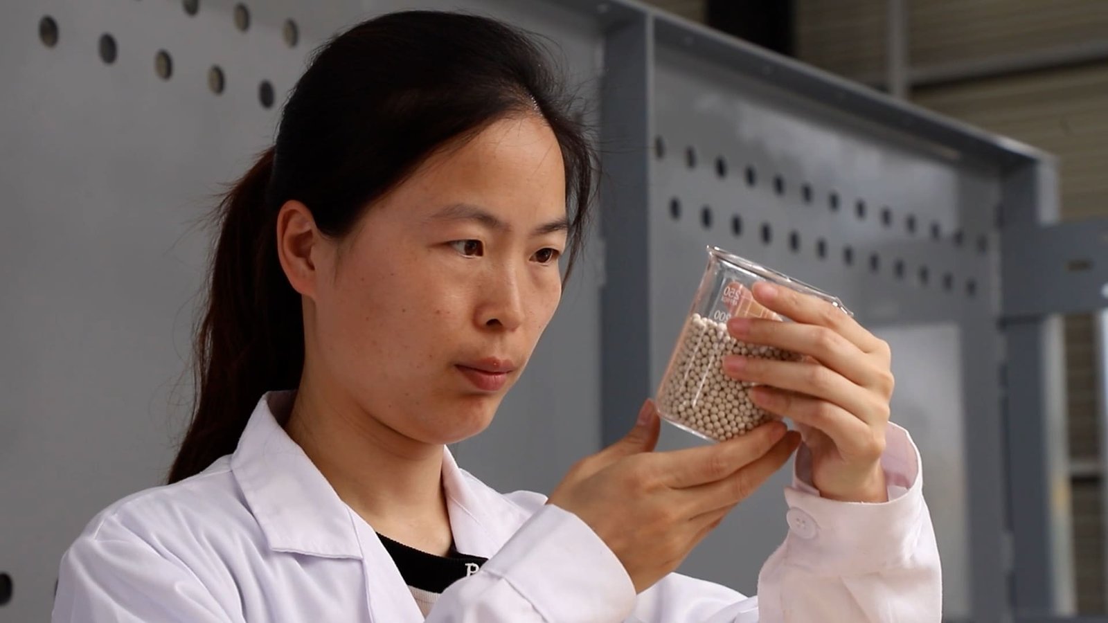 Two workers filling a large industrial tower with new molecular sieve, one pouring while the other taps the side of the tower.